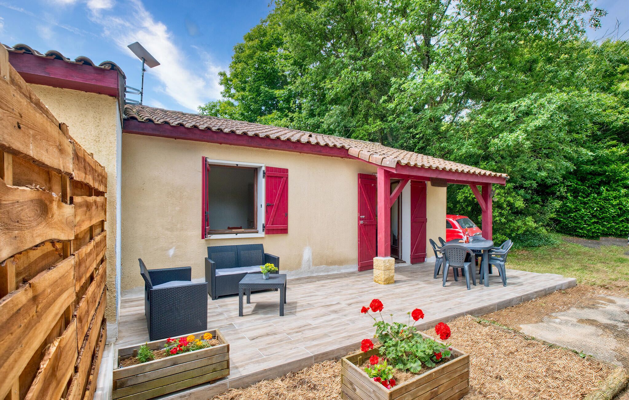 A small house with a patio, outdoor furniture, and a red car parked nearby.