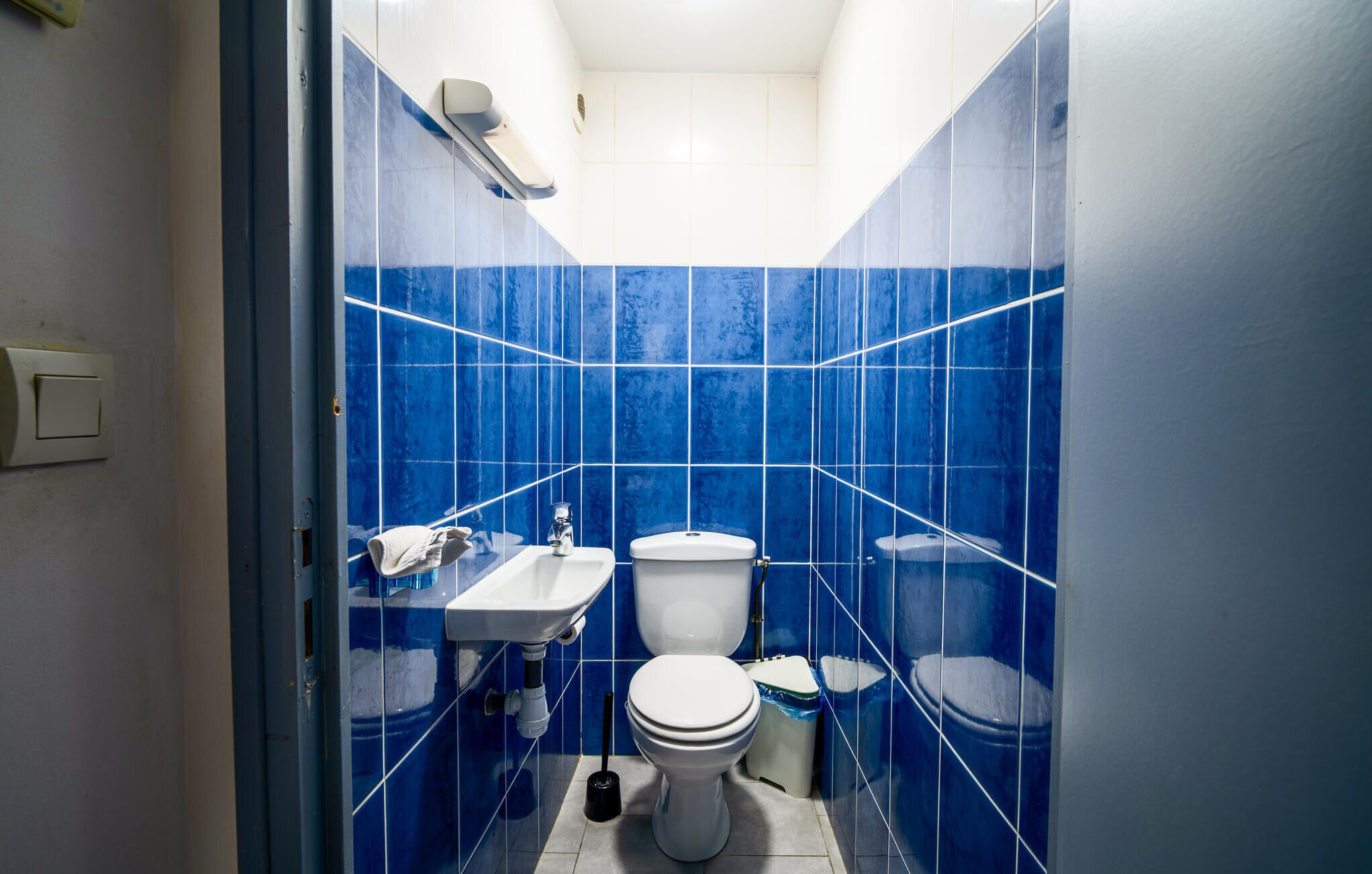 Ein kleines Badezimmer mit blauen Fliesen, einem weißen Waschbecken, einer Toilette und einem Mülleimer.