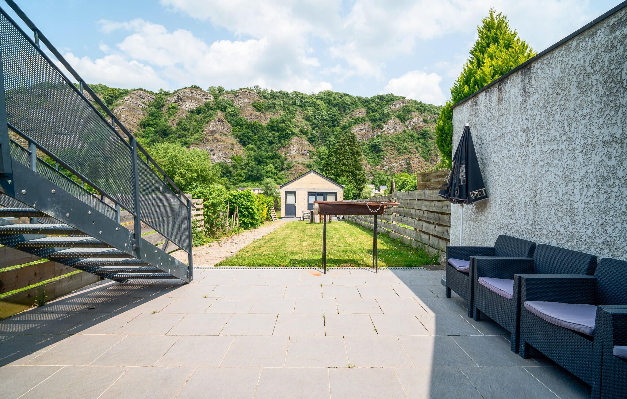 Zona patio con scala in metallo, posti a sedere all'aperto e vista su una casa e delle colline sullo sfondo.
