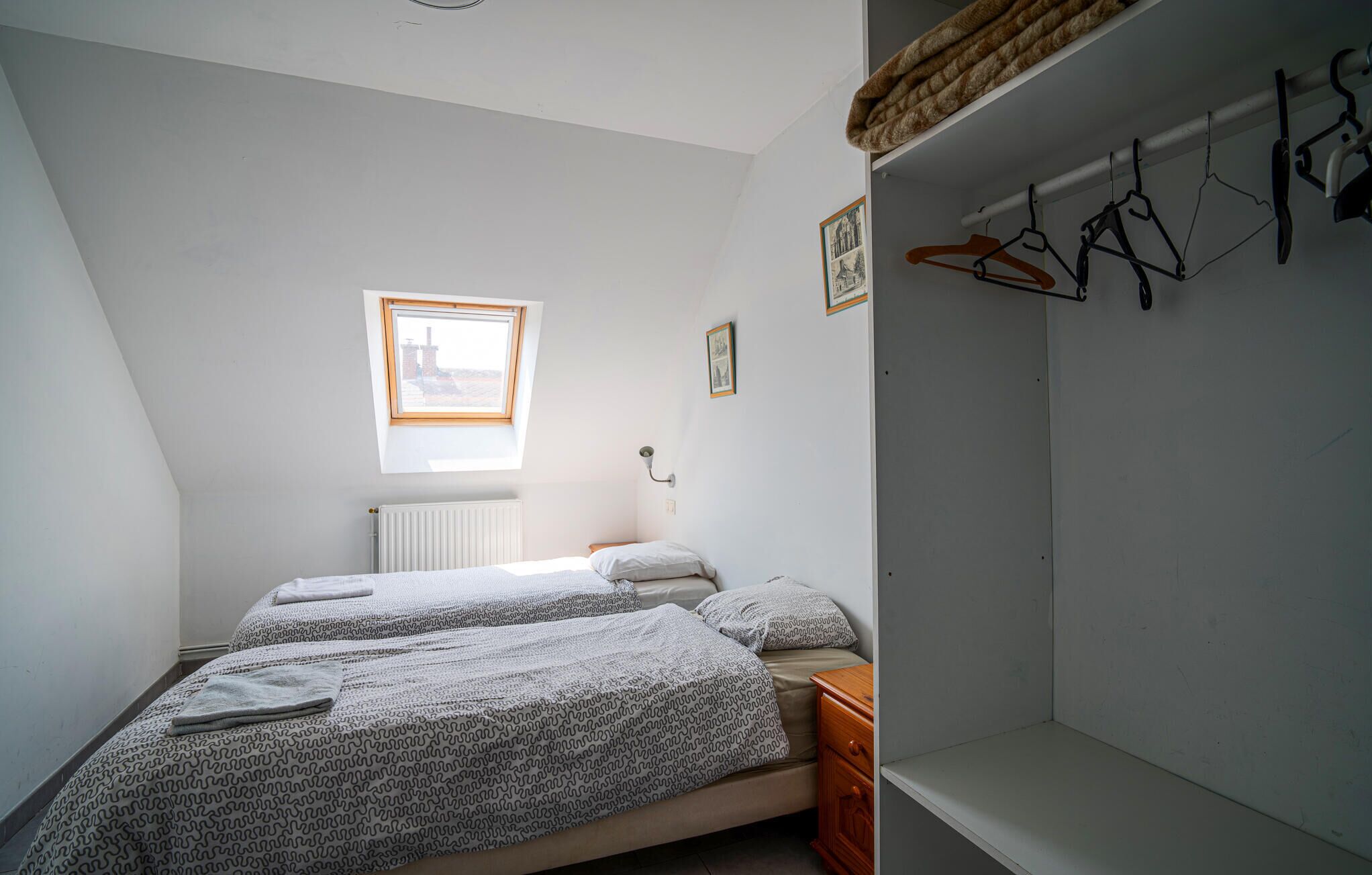 Un dormitorio con dos camas, un radiador, una ventana y un armario con perchas.