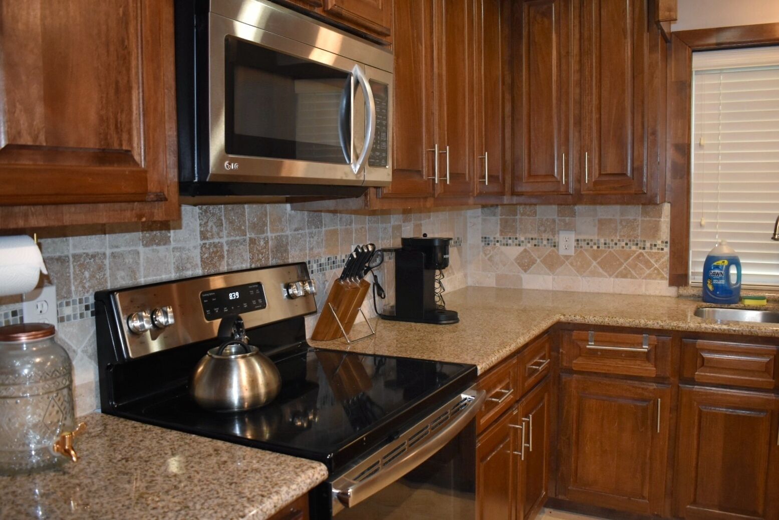 A kitchen with wooden cabinets, a stainless steel microwave, a stove, and a coffee maker.
