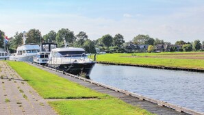 A canal with boats docked on the left, a grassy area, and houses in the background.