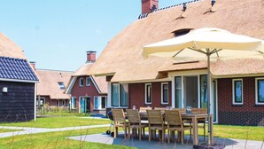 A row of thatched-roof cottages with outdoor dining areas, each featuring a table and chairs under a large umbrella.