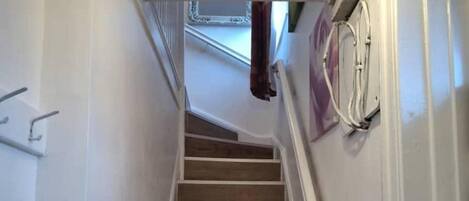 Un escalier étroit mène à un palier où se trouve une main courante sur la gauche et un appareil fixé au mur sur la droite.