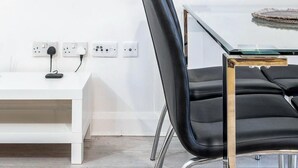 A modern room with a white console table, a black leather chair, and a glass-top table. There are three paintings on the wall and a flat-screen TV above the table. - Luxury Central London Balcony 1-Bed Apt w/ Parking (London)