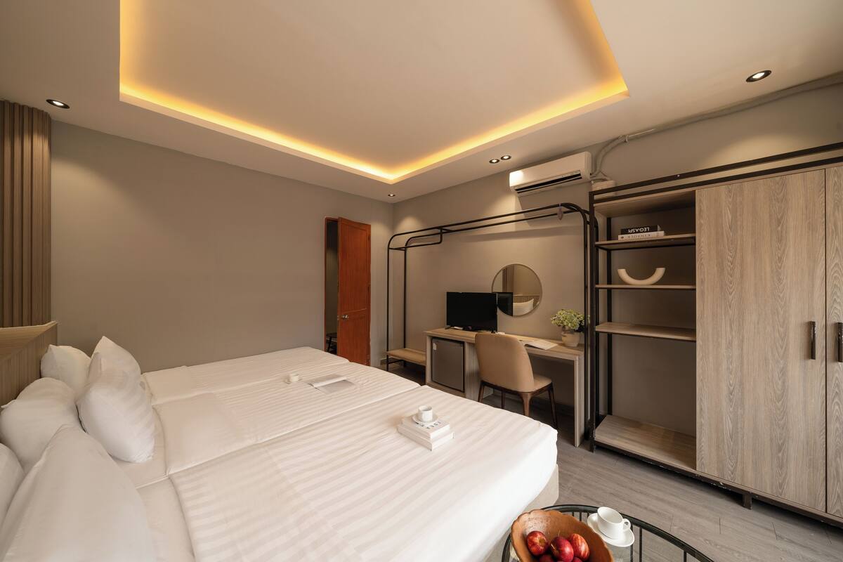 A modern hotel room with a large bed, a desk, a computer, and a wardrobe.