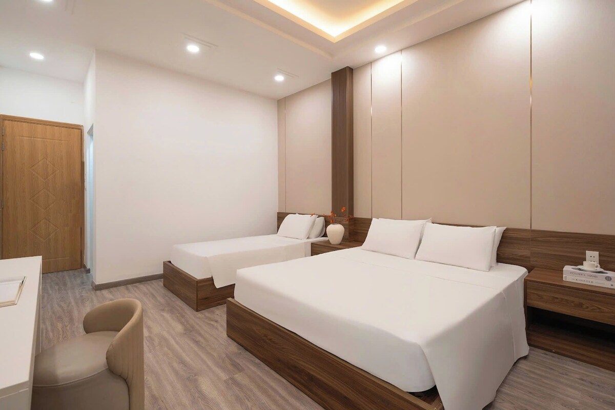 A hotel room with two beds, a desk, a chair, and a wooden wardrobe.