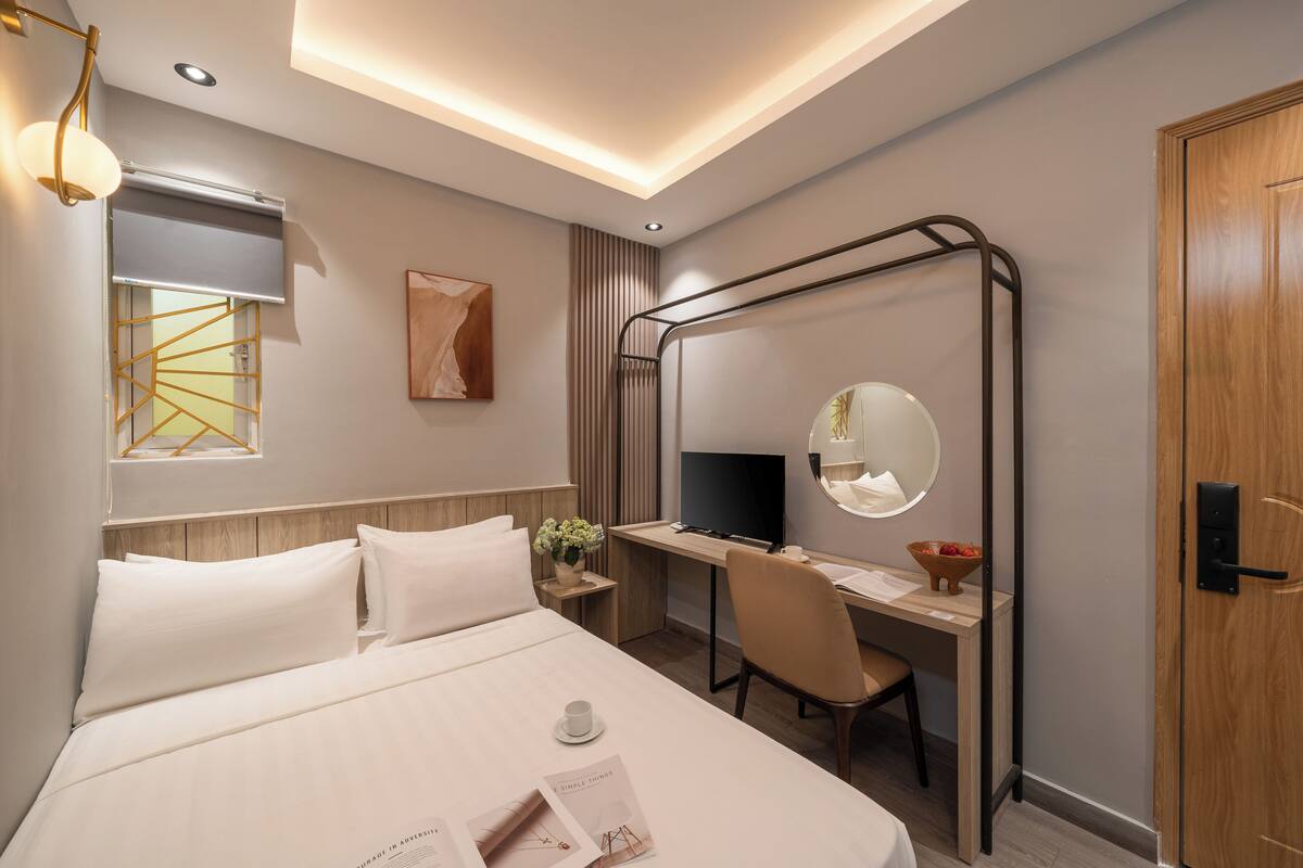 A modern hotel room with a bed, desk, chair, television, and a mirror.