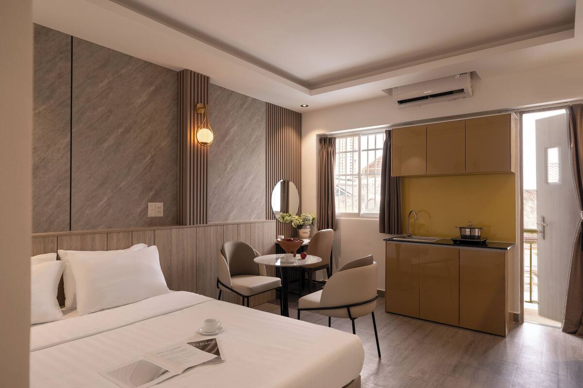 A hotel room with a bed, a small dining table, chairs, a kitchen area, and a large window.