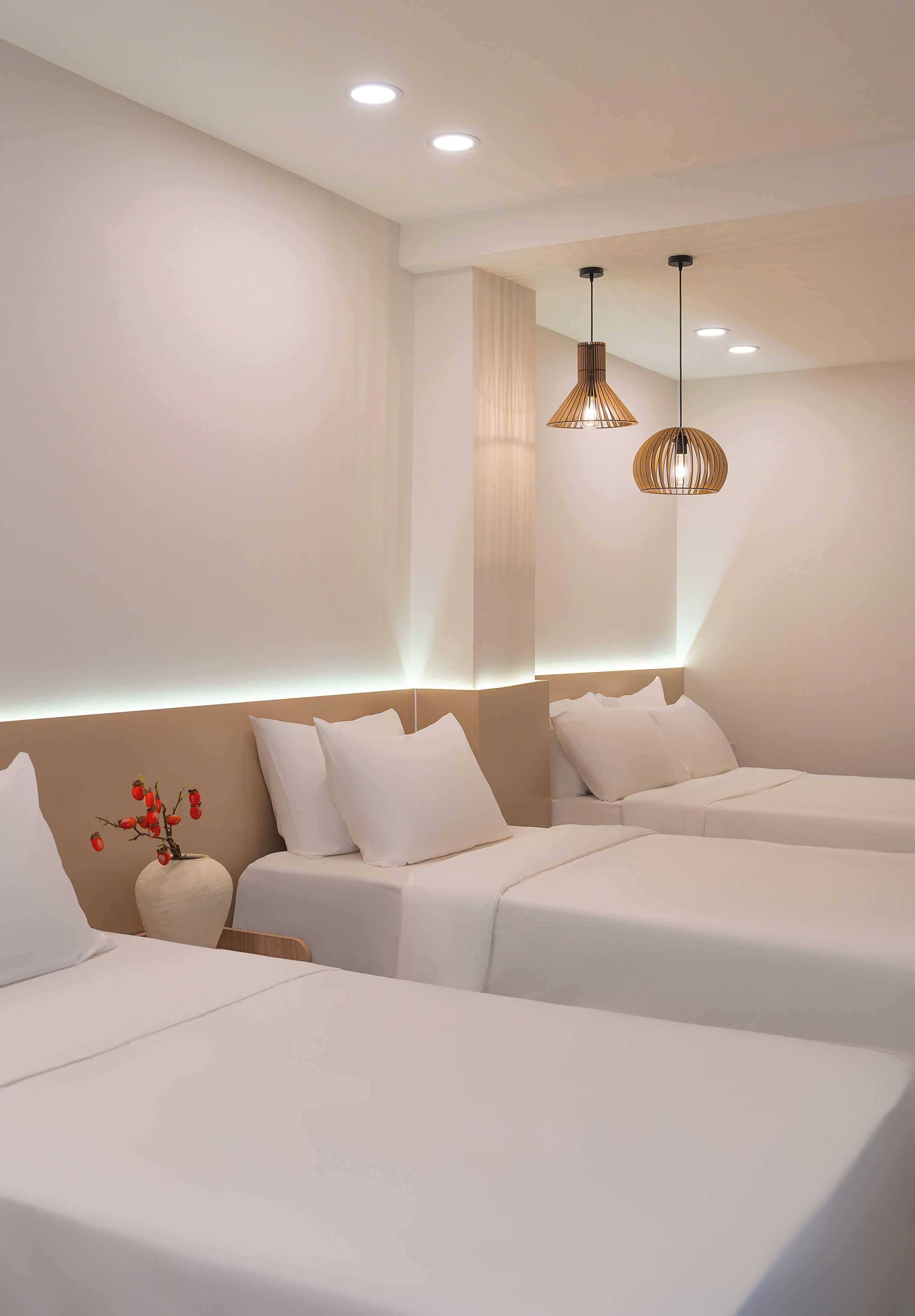A modern hotel room with two beds, a nightstand, and a decorative vase with red berries.