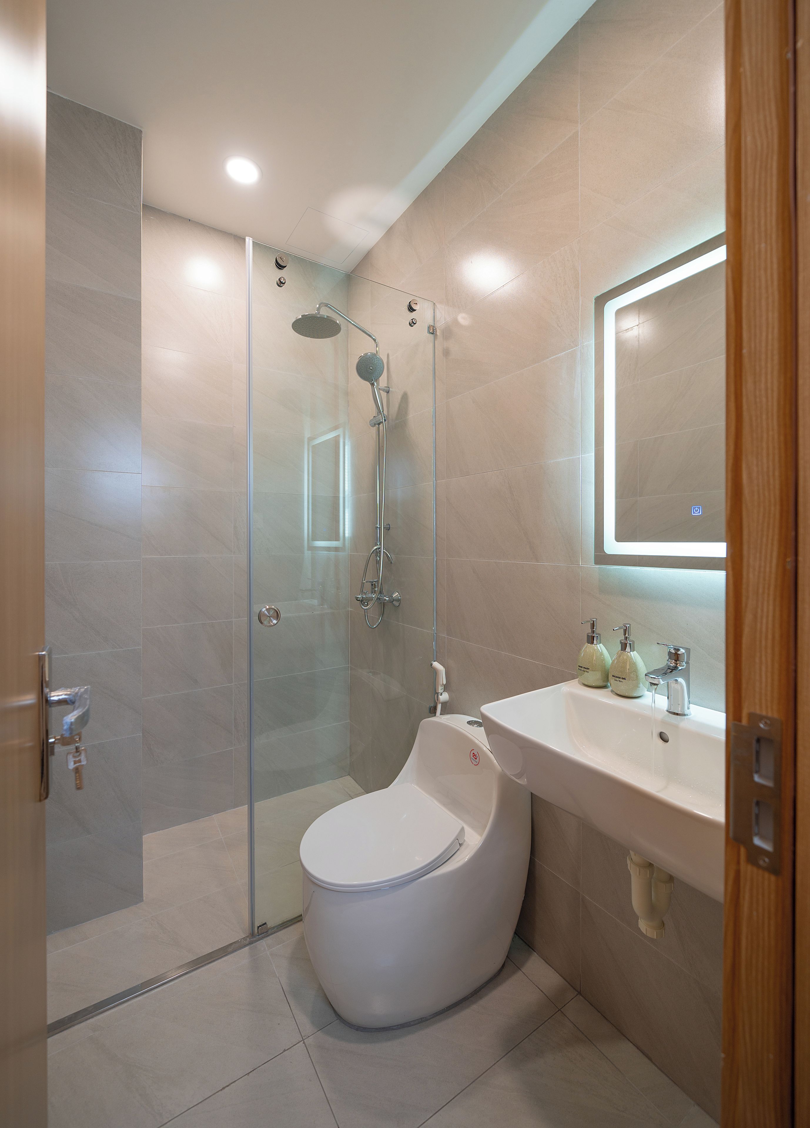 A modern bathroom with a glass-enclosed shower, a white toilet, and a sink with soap dispensers.