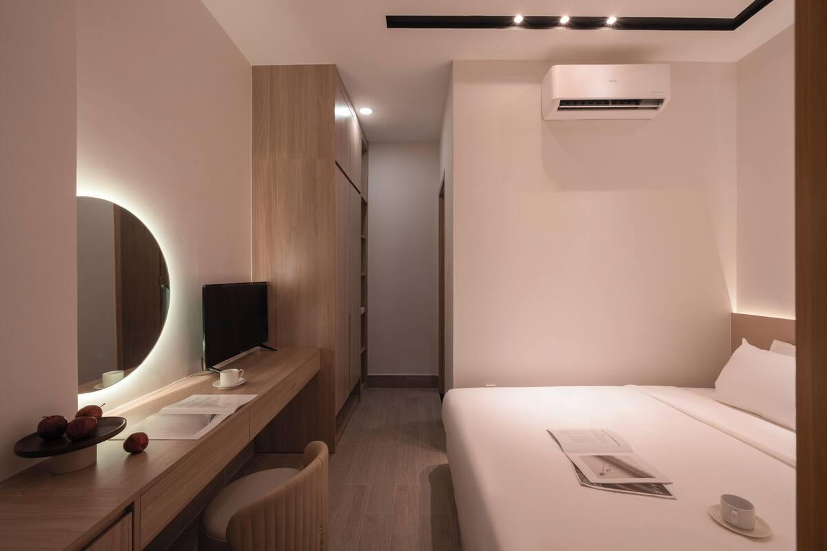 A modern hotel room with a wooden vanity, a bed, and a flat-screen TV.