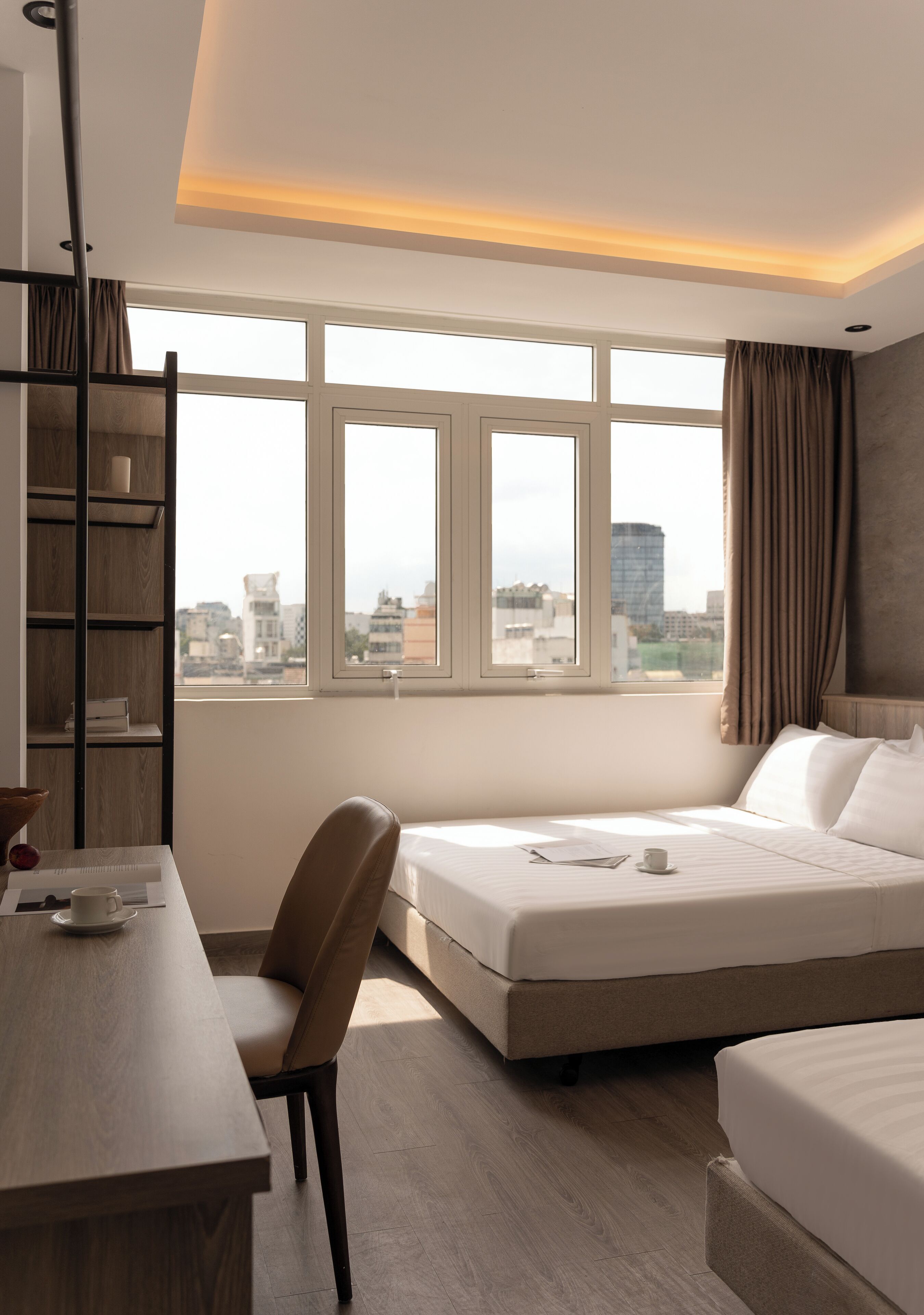 A hotel room with a bed, a desk, a chair, and a bookshelf.