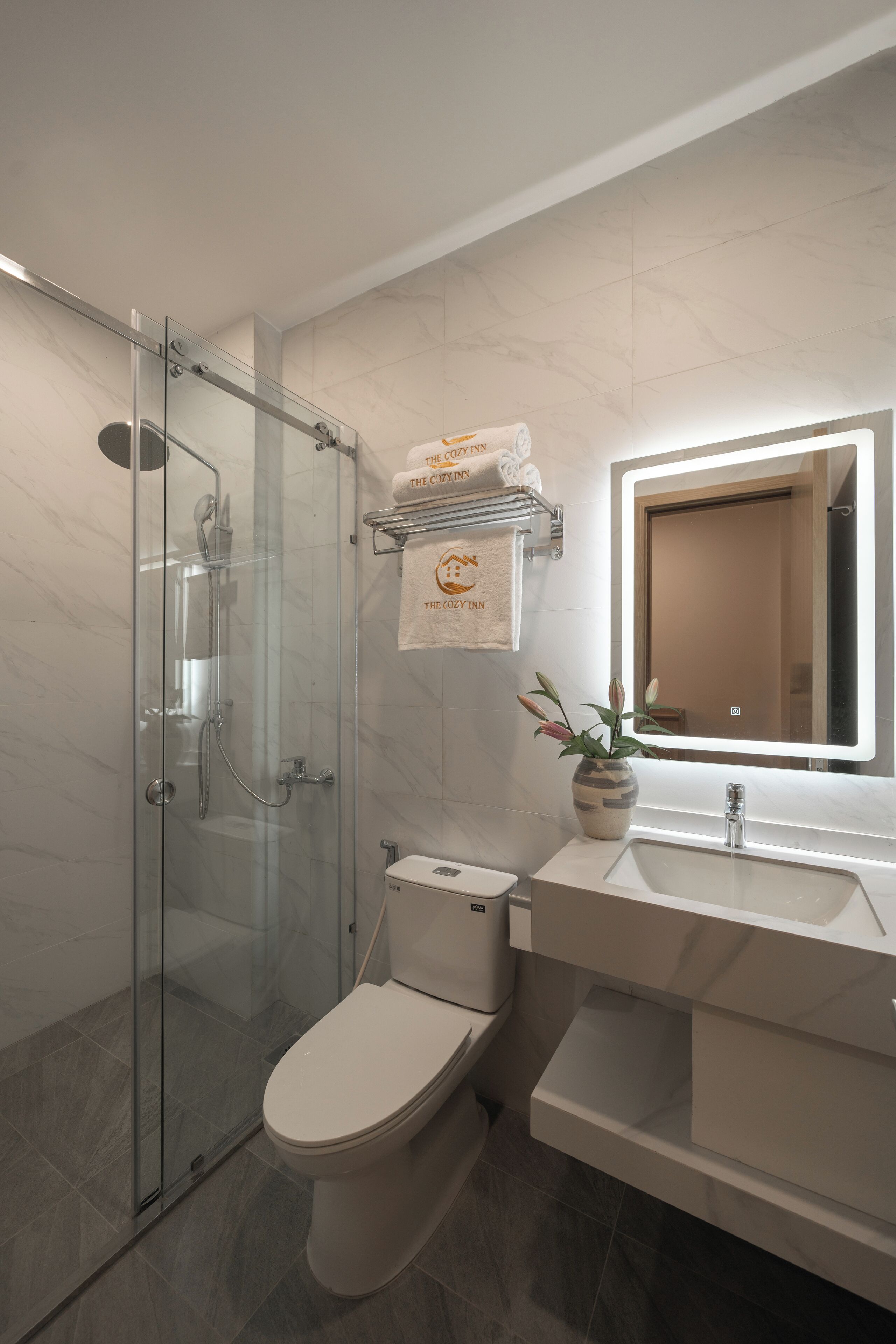 Une salle de bain moderne avec une douche à parois de verre, des toilettes blanches, un lavabo avec un miroir et un porte-serviettes avec des serviettes de marque.