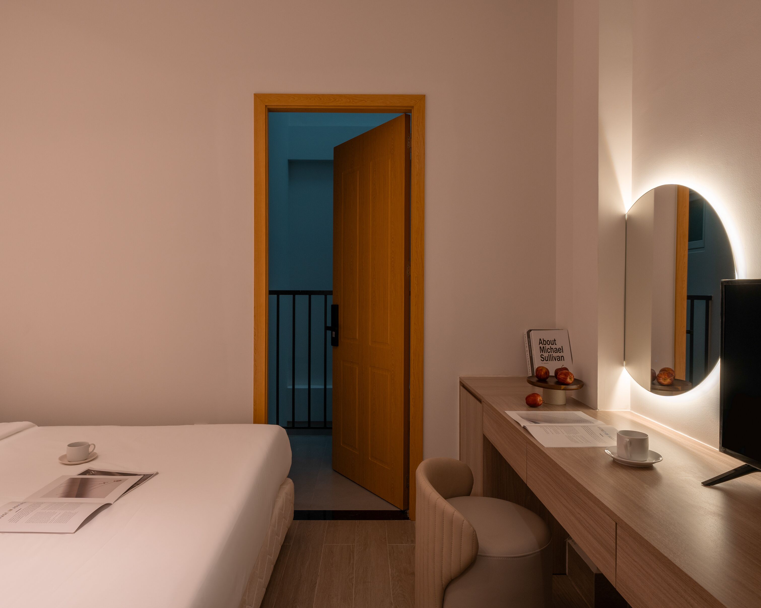 A hotel room with a bed, a desk with a mirror, a chair, and a small table with a sign.