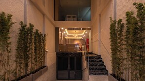 A modern building entrance with a staircase, glass doors, and indoor plants. - The Cozy Inn Ho Chi Minh (Ho Chi Minh City)