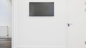 Ein Zimmer mit einem an der Wand befestigten Flachbildfernseher, einer weißen Tür mit violettem Griff und einem weißen Heizkörper am Boden.