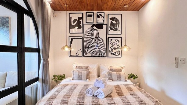 Une chambre moderne avec un plafond en bois, un grand lit recouvert d’une courtepointe à rayures et des œuvres d’art accrochées au mur.