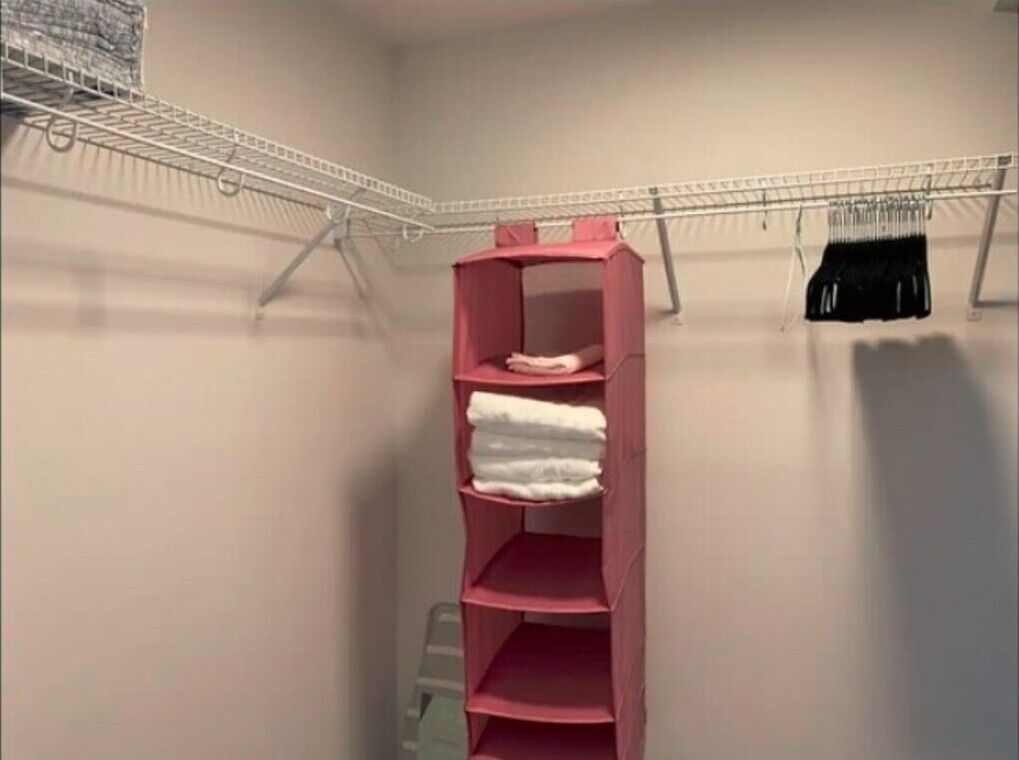 A room with a pink shelving unit against a wall, a metal rack with clothes, and a white wall.