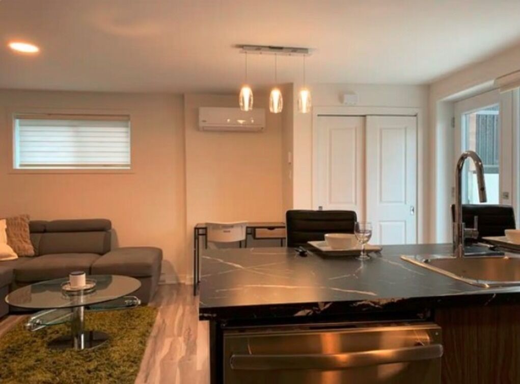 A modern kitchen with a marble countertop, a built-in oven, and a sink. There is a dining area with a table and chairs, and a living room with a sofa and a coffee table.