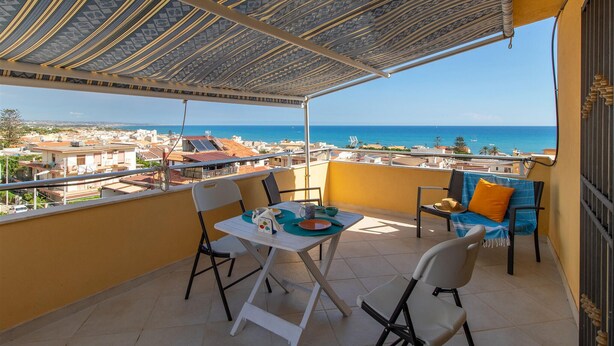 A balcony with a table and chairs, overlooking a coastal view. - Beautiful apartment in Marina di Ragusa with house sea view (Marina di Ragusa)