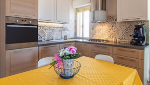 A modern kitchen with a built-in oven, a coffee machine, and a window with curtains. - Beautiful apartment in Marina di Ragusa with house sea view (Marina di Ragusa)