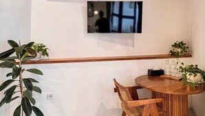 Une pièce avec un plafond en bois, une table ronde en bois entourée de chaises, une petite plante en pot et un appareil de climatisation fixé au mur.