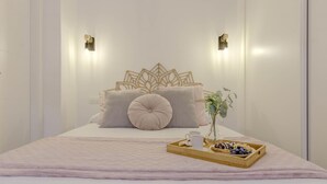 Un lit bien fait, agrémenté d’une tête de lit décorative, une tablette avec des biscuits et une tasse, et deux appliques murales.
