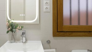 Une salle de bain avec un lavabo blanc, un miroir, des toilettes et une fenêtre en verre dépoli.