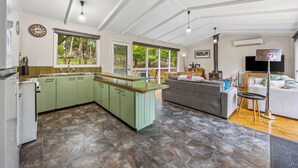 A spacious living area with a kitchen, large windows, and a fireplace. - High Road Haven (Halls Gap)