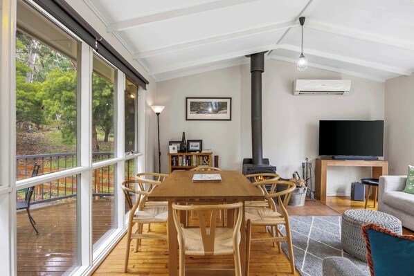 Un salón amplio con una gran mesa de madera, asientos cómodos, una chimenea, un televisor y vistas al exterior.