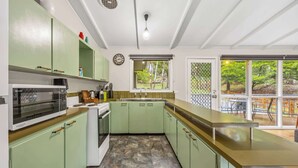 A kitchen with green cabinets, a microwave, a sink, and a window overlooking a garden. - High Road Haven (Halls Gap)