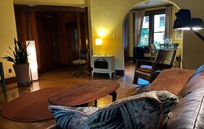Un salón acogedor con suelo de madera, un sofá de cuero marrón, un sillón estampado, una mesita de madera y una lámpara en una mesita auxiliar.