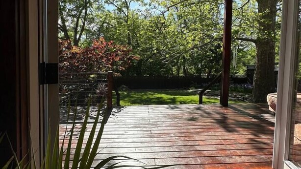 A wooden deck with a pair of sandals on it, leading to a covered outdoor area with a view of trees and a lawn.