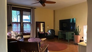 A living room with a wooden floor, a ceiling fan, a TV, a dining table with chairs, and a sofa.