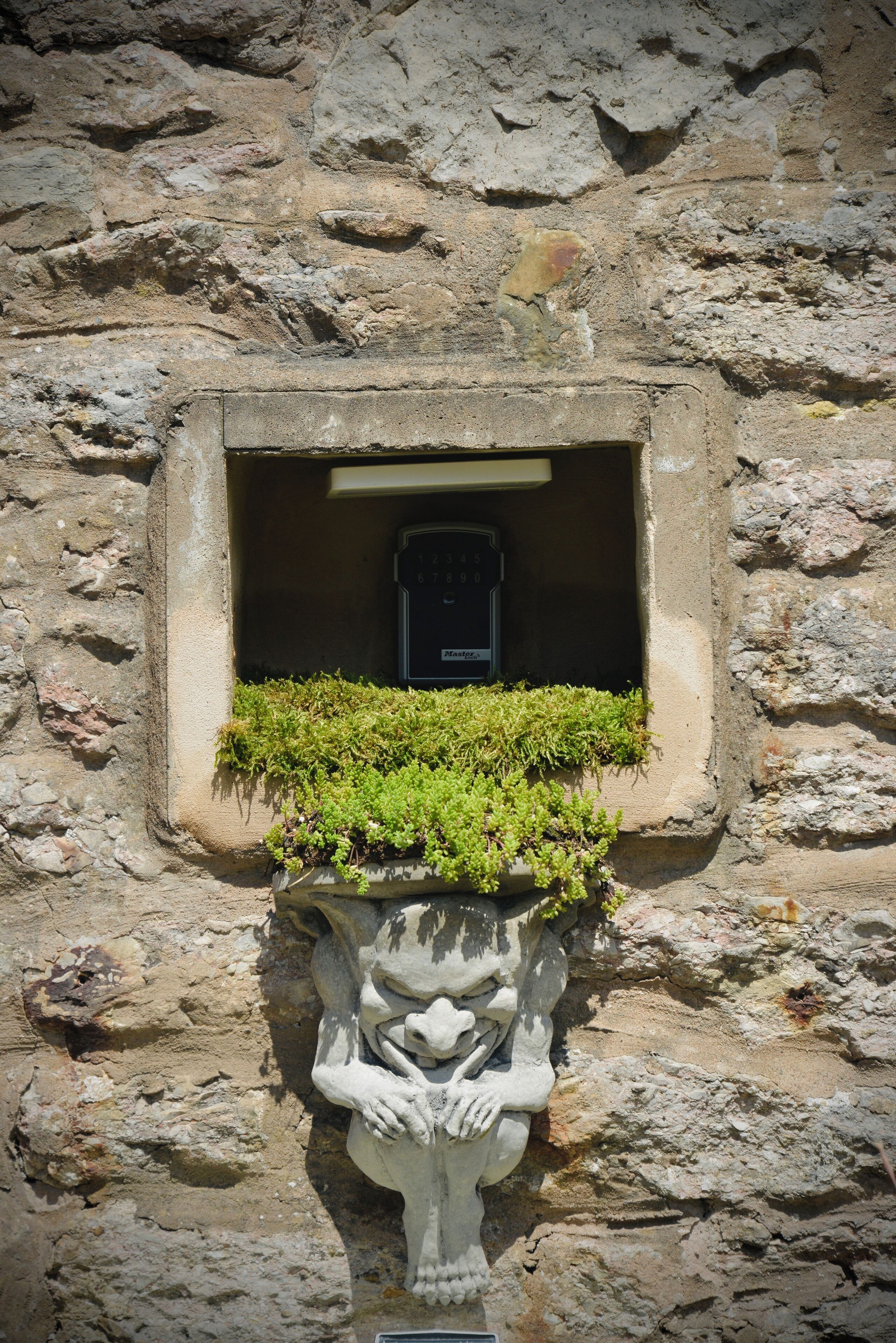 A stone wall with a window featuring a small plant and a decorative stone figure.