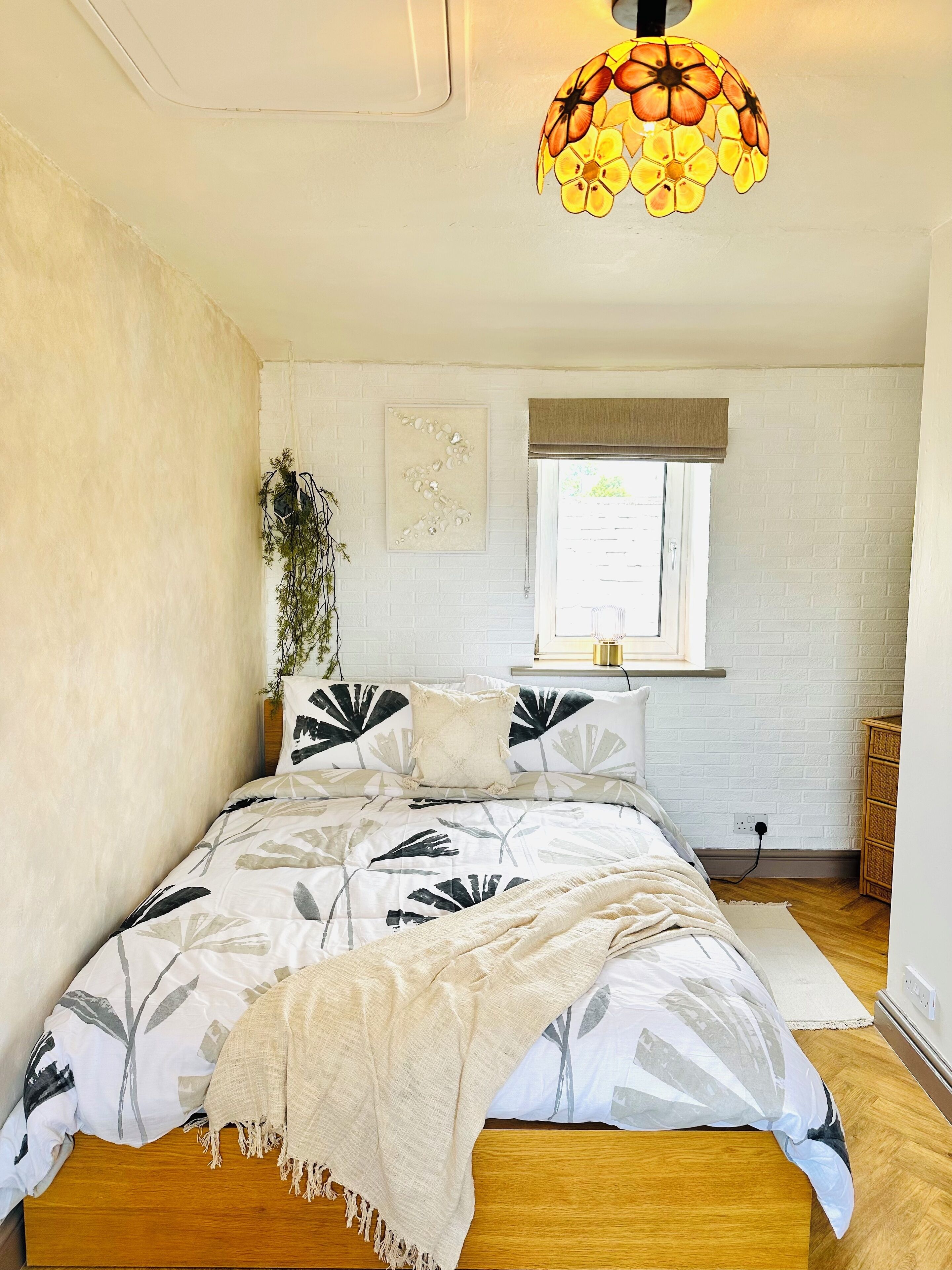 Quarto com cama, janela, planta fixada na parede e luminária no teto.