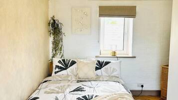 Quarto com cama, janela, planta fixada na parede e luminária no teto.