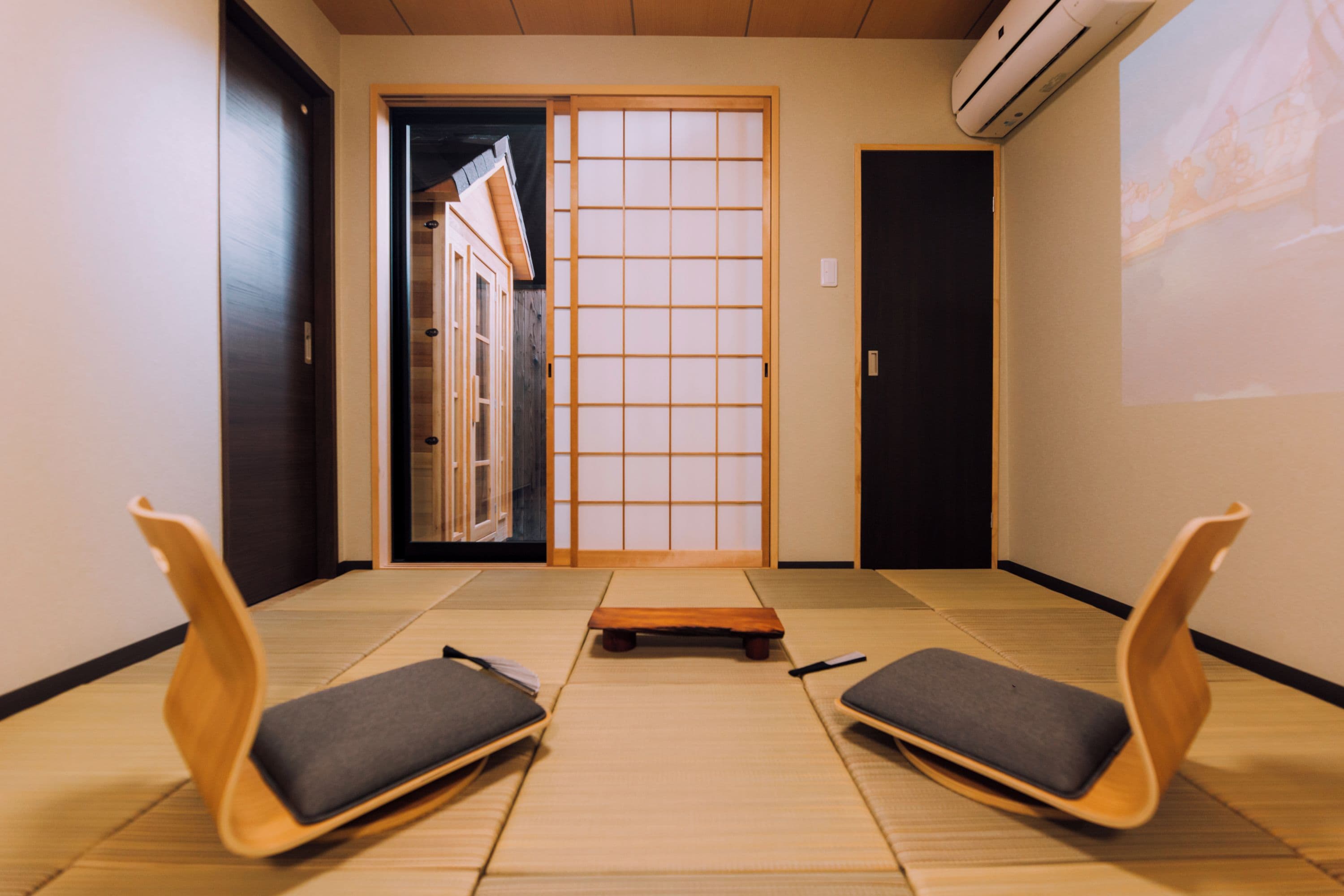 A traditional Japanese room with tatami flooring, a shoji screen door, and two tatami mats with cushions.