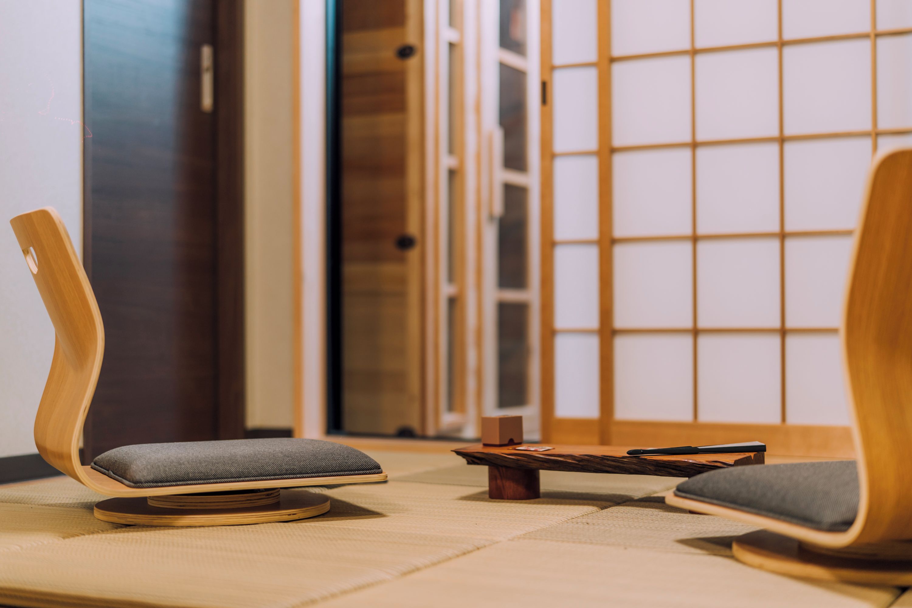 A room with two wooden chairs with cushions, a small wooden table, and a sliding door with a grid pattern.