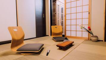 A traditional Japanese room with tatami flooring, a wooden chair, a small table, and a vase with flowers.