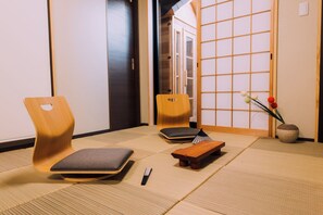 A traditional Japanese room with tatami flooring, a wooden chair, a small table, and a vase with flowers. - mist Osaka - Private Outdoor Sauna & Projector (Osaka)