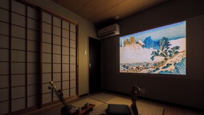 Una habitación japonesa tradicional con suelo de tatami, un biombio shoji y una pantalla de proyección que muestra un paisaje.