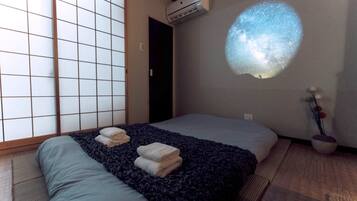 A room with a bed, a futon, a sliding shoji screen, a projector, and a small plant.