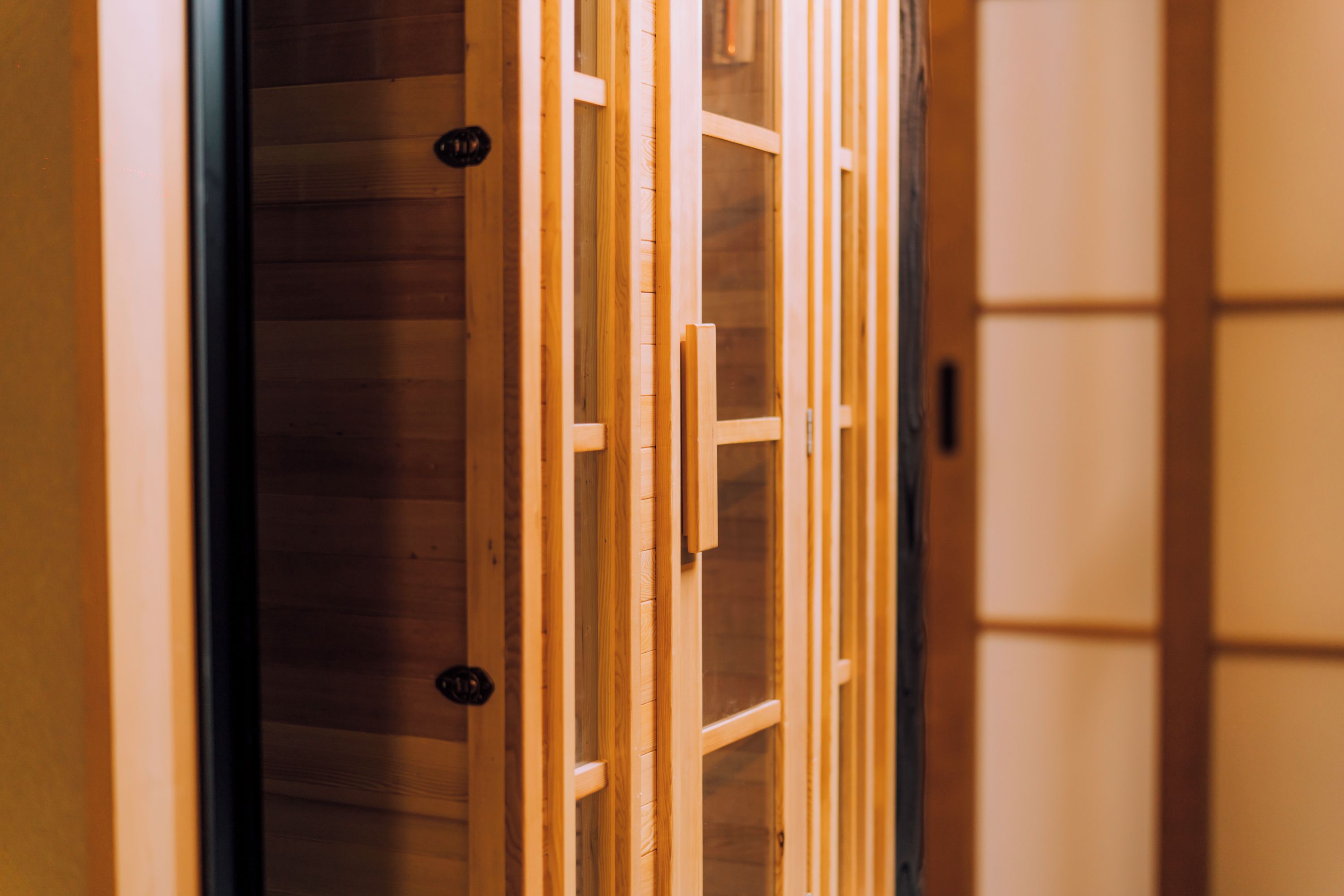 A wooden interior with a sliding door and a view into a room with a wooden floor.