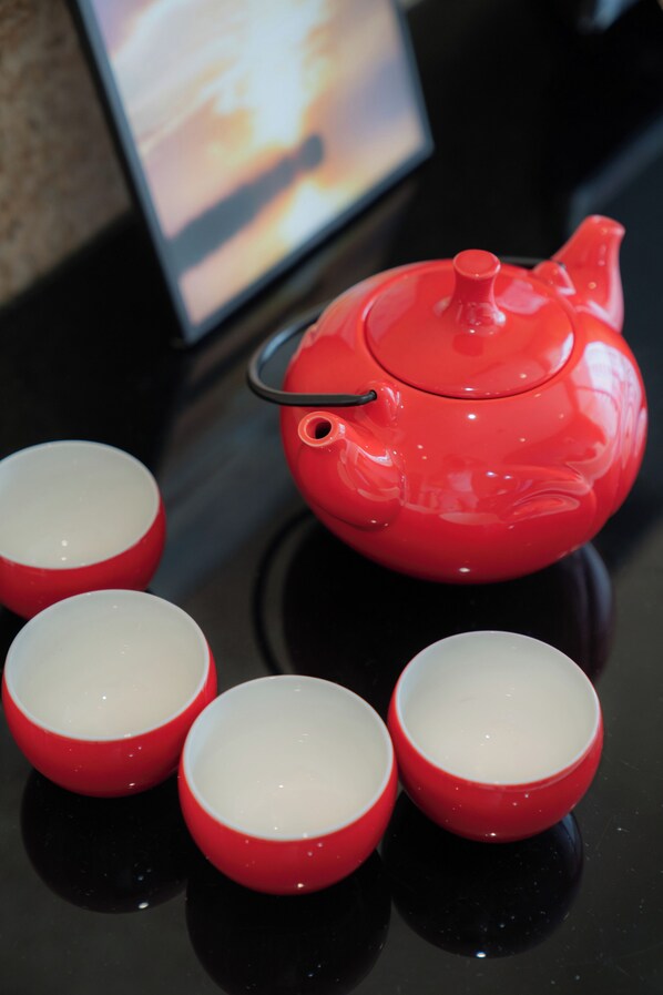 A red teapot and four matching cups on a reflective black surface.