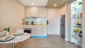 A modern kitchen with light wood cabinets, a built-in oven, and a refrigerator. There is a dining table set with plates, cups, and a vase of flowers. - Seven Seas Condo Resort steps to  Beach (Pattaya)