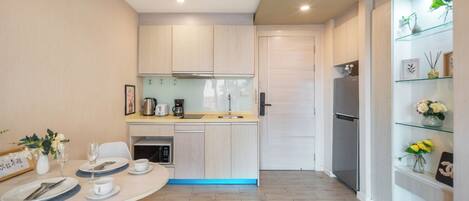 Una cocina moderna con armarios de madera clara, horno integrado y refrigerador. Hay una mesa de comedor con platos, tazas y un jarrón de flores.