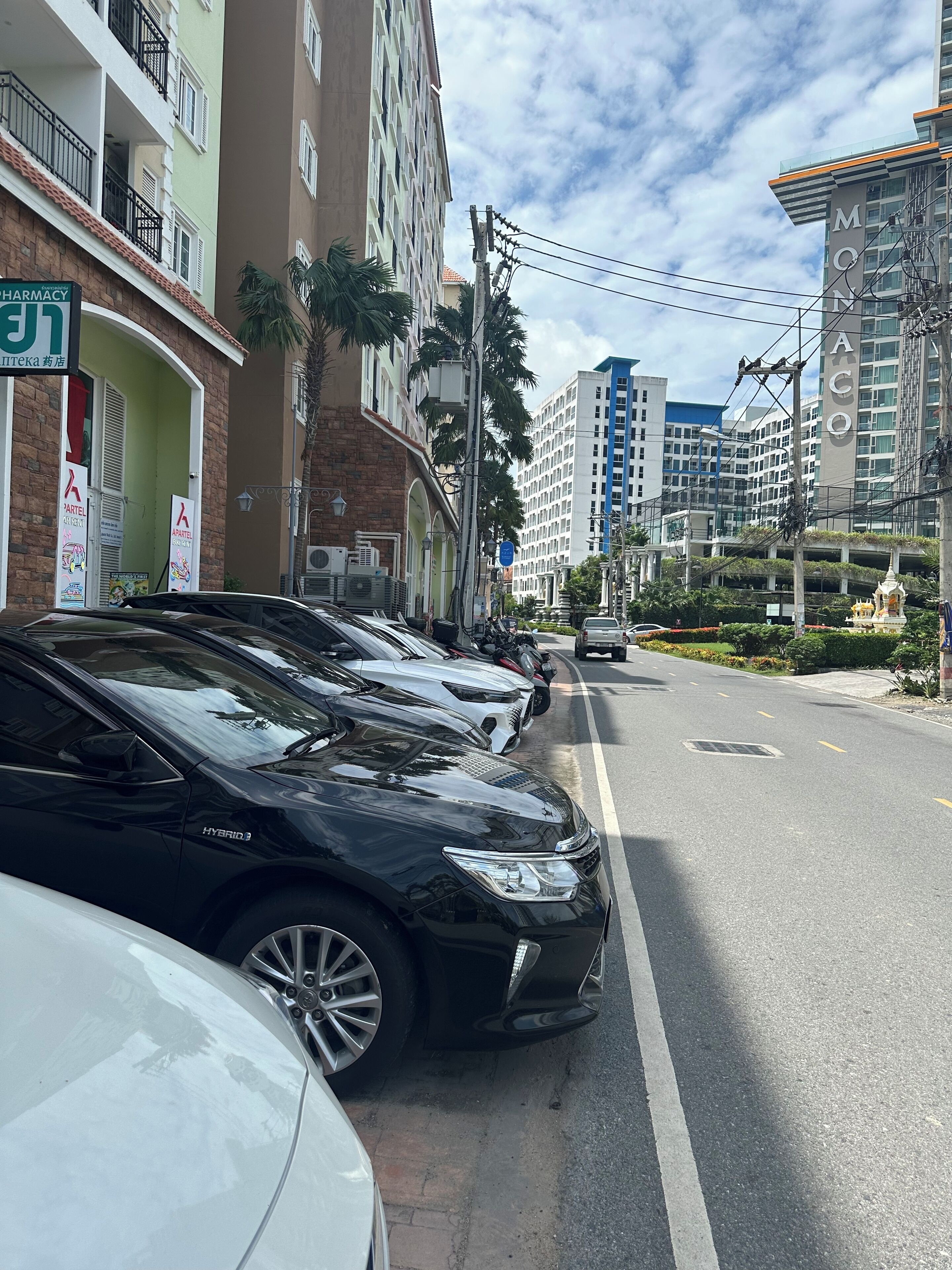 Una fila de coches aparcados a lo largo de una calle urbana, con edificios de varios pisos al fondo.