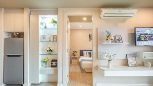 A modern kitchen with a built-in refrigerator, a dining area with a white countertop, and a bedroom with a bed and a nightstand. - Seven Seas Condo Resort steps to  Beach (Pattaya)